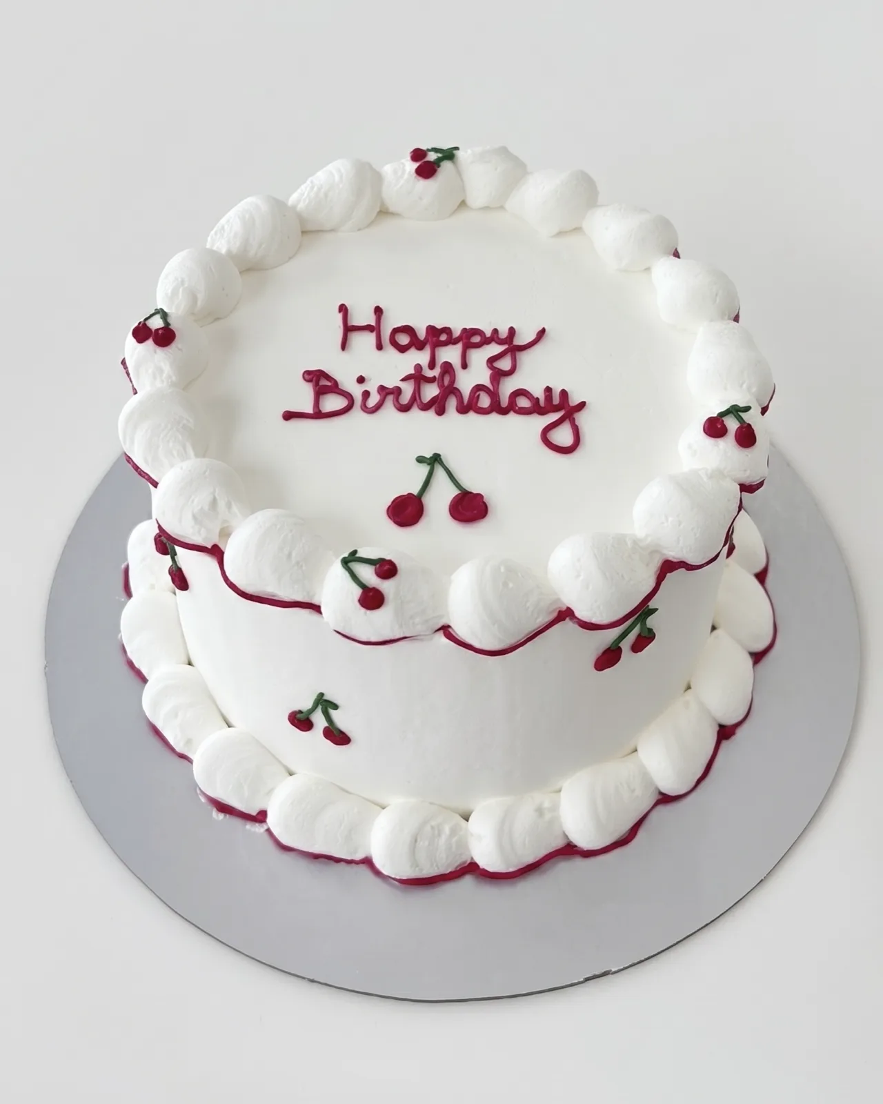 Minimal white birthday cake with a piped border and hand-painted cherries, a custom cake by Cakes By Vjollca in Pristina, Kosovo