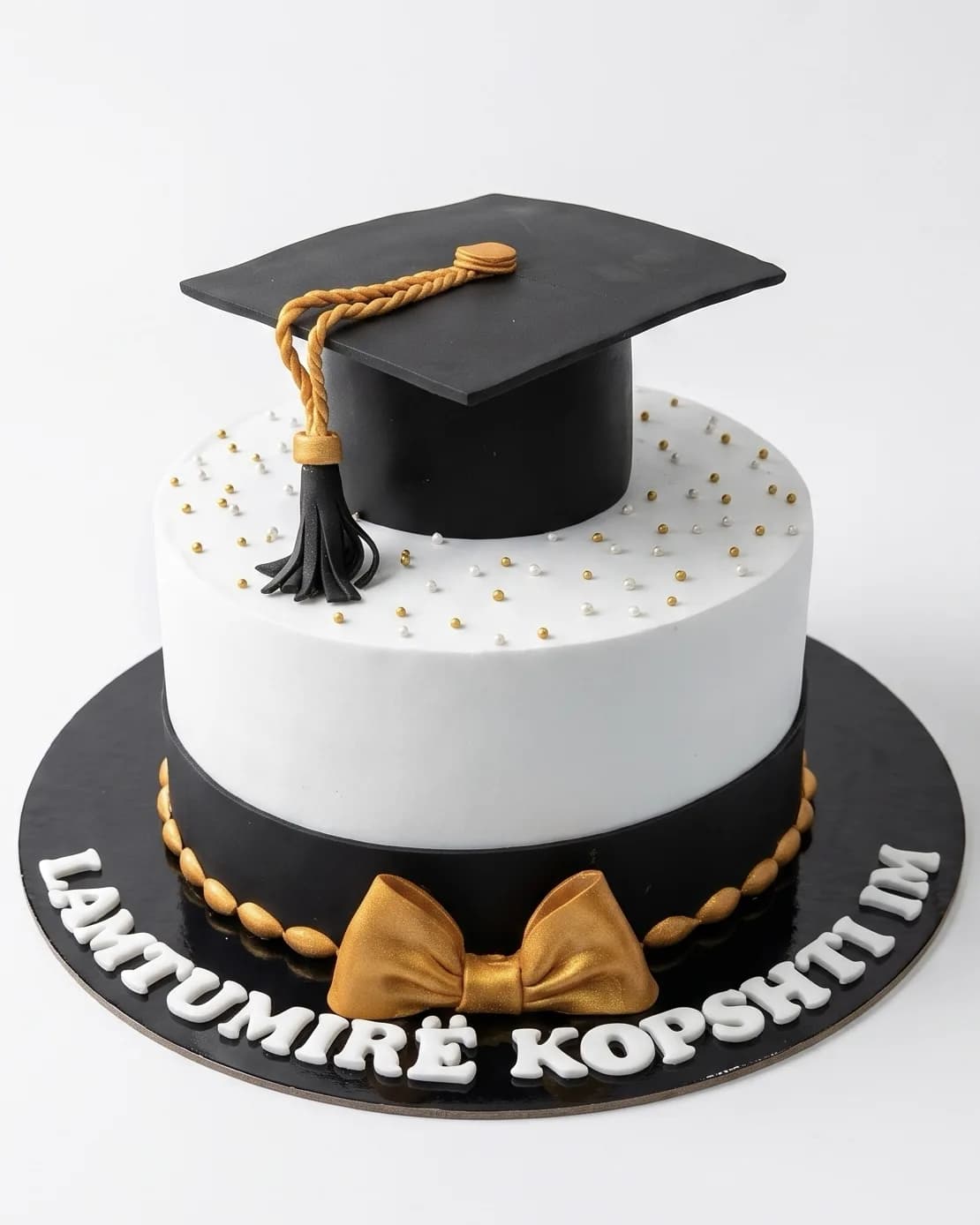 Black and white graduation cake with a fondant graduation cap and gold bow, a custom cake by Cakes By Vjollca in Pristina, Kosovo