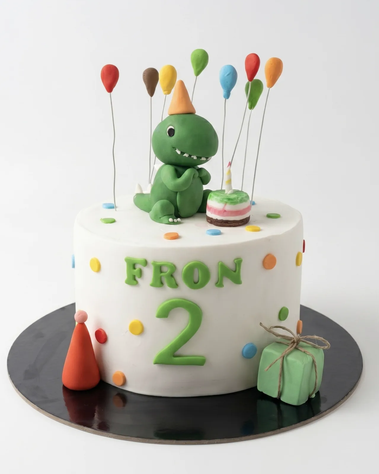 White birthday cake with a dinosaur figurine, balloons and confetti dots, a custom cake by Cakes By Vjollca in Pristina, Kosovo