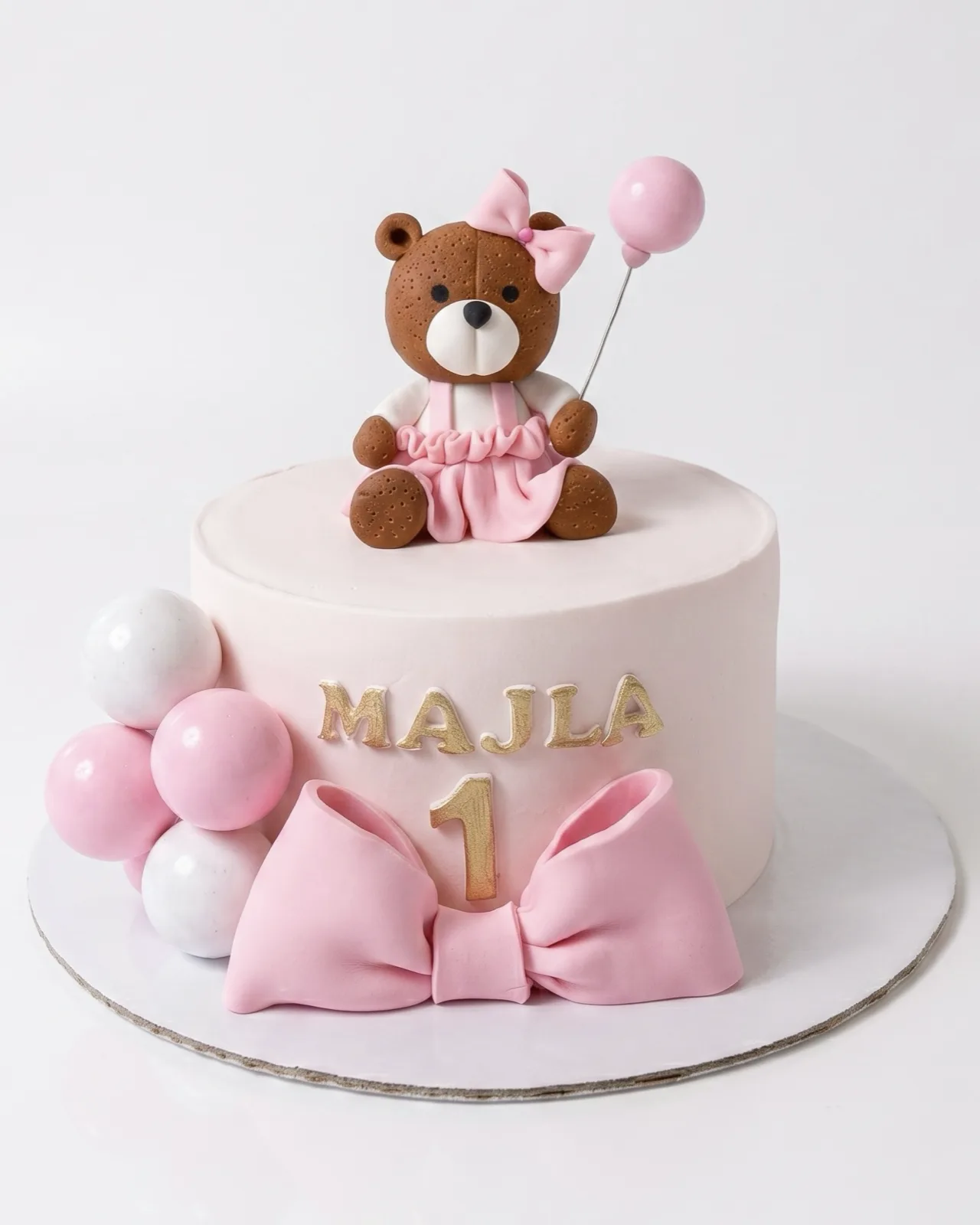Blush first birthday cake with a teddy bear, pink bow and balloons, a custom cake by Cakes By Vjollca in Pristina, Kosovo