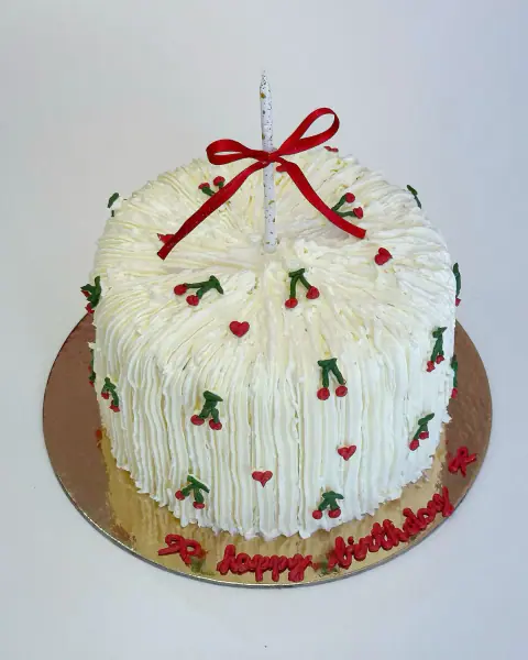 White buttercream birthday cake piped in vintage style with cherries, hearts and a ribbon-tied candle, a custom cake by Cakes By Vjollca in Pristina, Kosovo