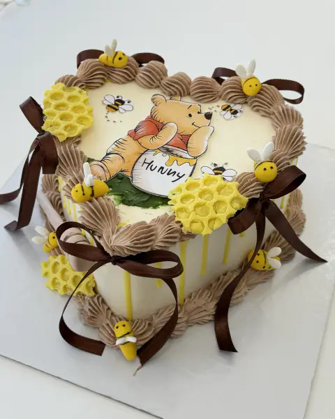 Winnie the Pooh heart cake with honeycomb, bees and chocolate bows, a custom cake by Cakes By Vjollca in Pristina, Kosovo