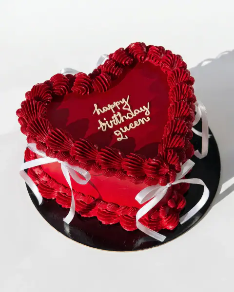 Red heart-shaped birthday cake piped in vintage style with white satin ribbons and hand-written lettering, a custom cake by Cakes By Vjollca in Pristina, Kosovo