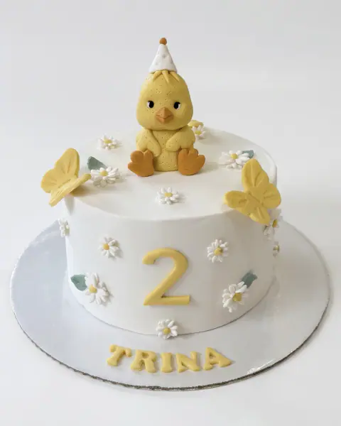 White second birthday cake with a duckling topper, daisies and butterflies, a custom cake by Cakes By Vjollca in Pristina, Kosovo